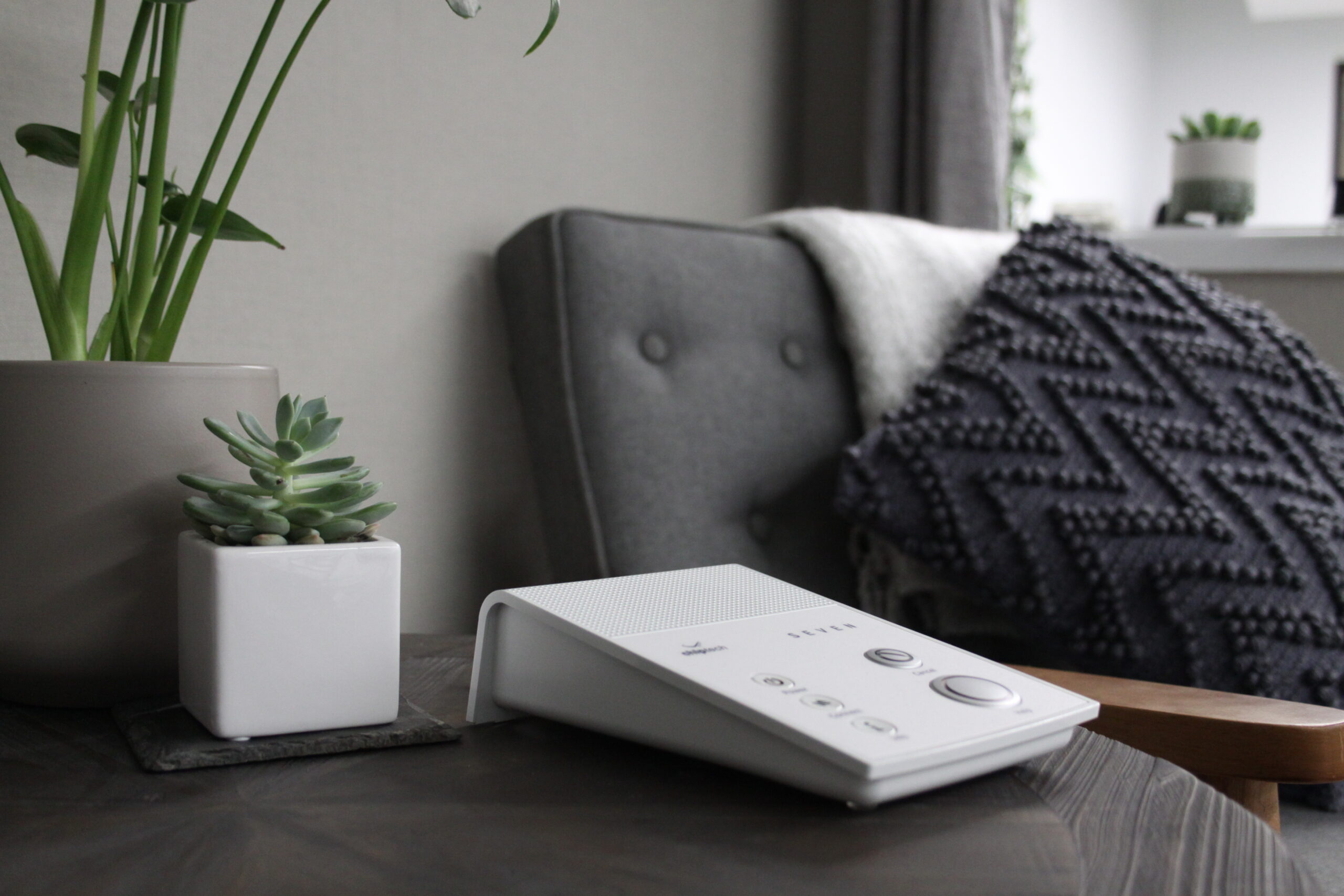 El dispositivo SEVEN de Chiptech sobre una mesa en el salón, con una planta en maceta a la izquierda y una silla gris al fondo