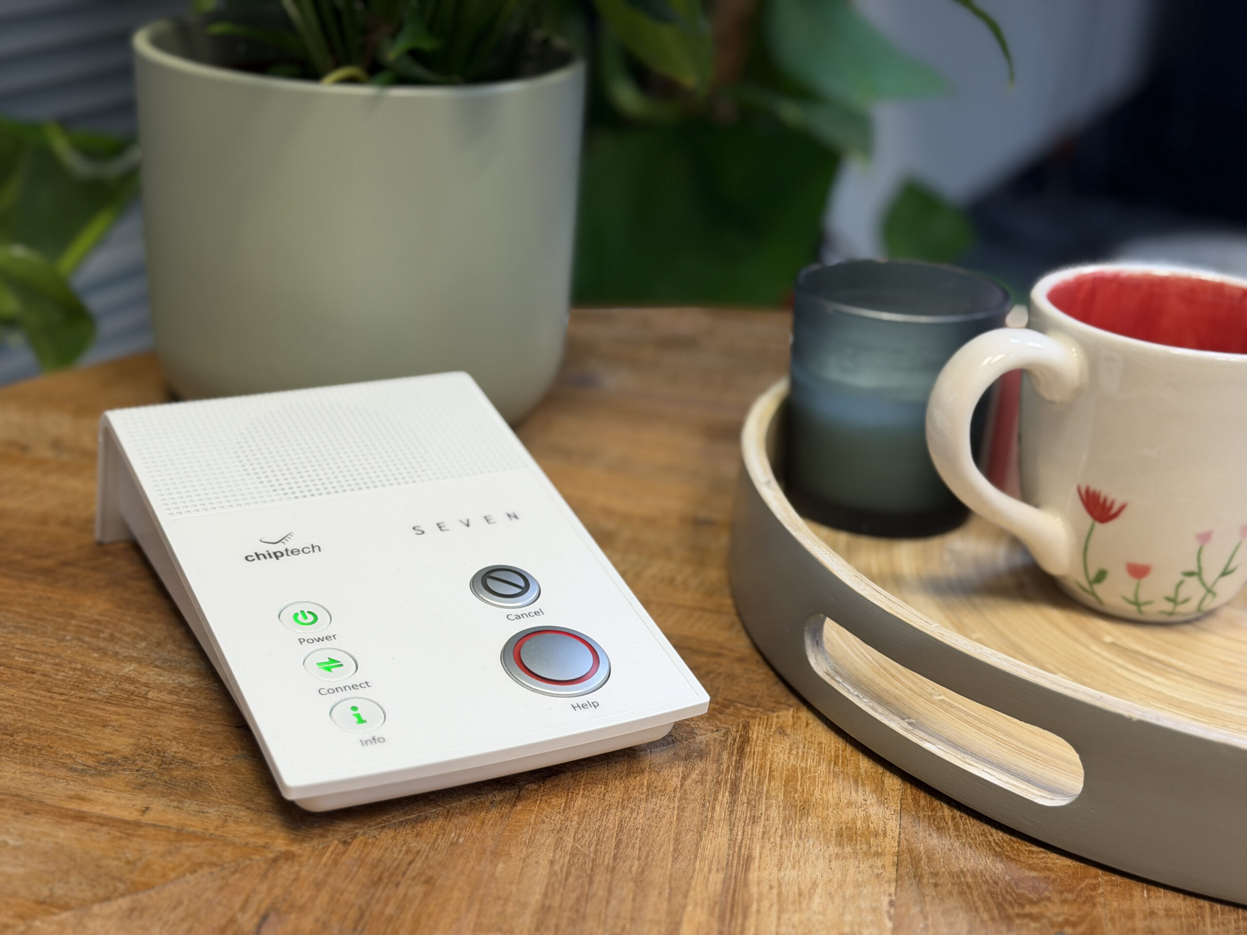 Chiptech's SEVEN base unit sits on a wooden living room coffee table, with a potted plant and tray of mugs alongside it.